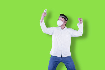 Portrait of young man with arms raised against green background