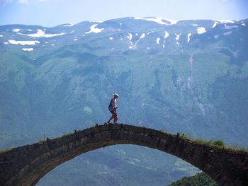 Woman walking with daughter on bridge by mountain against sky