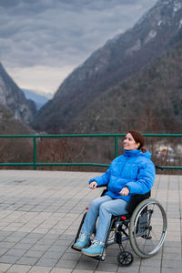 Portrait of woman sitting on railing against mountain