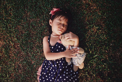 Directly above shot of girl with teddy bear lying on field