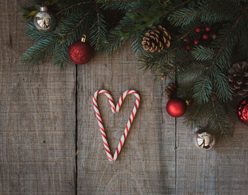 Candy canes in a heart shape on wooden table with christmas decor.