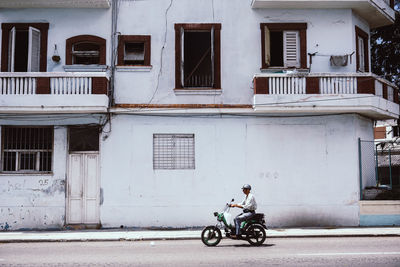 Side view of man cycling on street against building