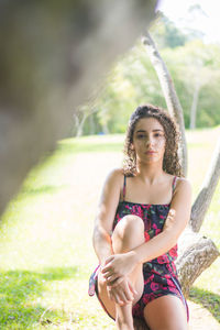 Portrait of serious young woman sitting on tree trunk in park