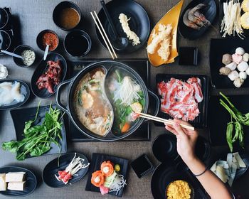 Cropped image of woman picking food from hot pot on table