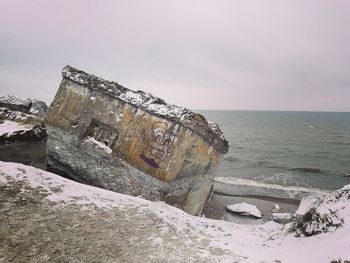 Abandoned snow covered land by sea against sky