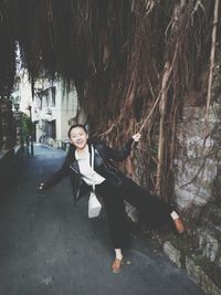 Portrait of cheerful woman holding banyan tree vine on footpath
