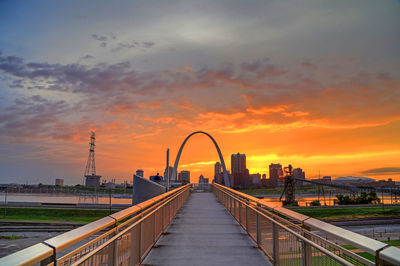 Bridge over river and buildings against sky during sunset