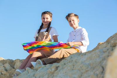 A boy and a girl collect a kite sitting on a stone on a sunny summer day.