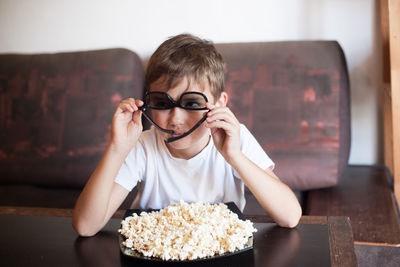 A boy in 3d glasses watches a movie and eats popcorn with his mouth wide open sitting on the couch