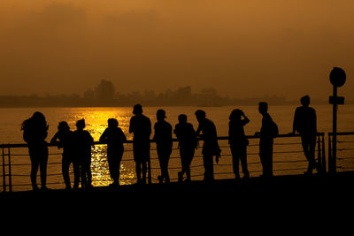 Silhouette people standing by sea against sky during sunset