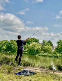 Rear view of man standing by lake against sky