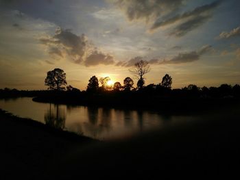 Silhouette trees by lake against sky during sunset