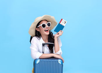 Young woman wearing sunglasses standing against blue background