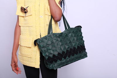 Midsection of woman holding bag against gray background