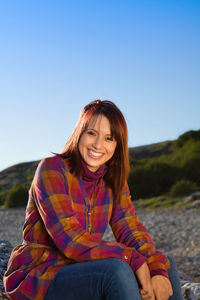 Portrait of smiling young woman sitting against sky