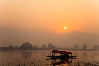 Silhouette boat in lake against sky during sunset