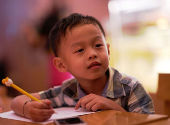 Cute boy writing in book while sitting at table