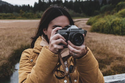 Portrait of young woman taking photos of autumn nature with vintage camera