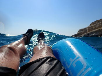 Low section of man on inflatable boat in sea against clear blue sky