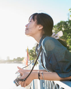 Side view of young woman holding sunglasses against sky