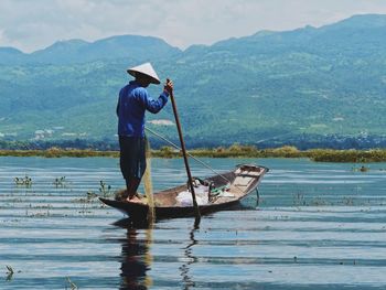 Fisherman sailing boat in lake against mountains