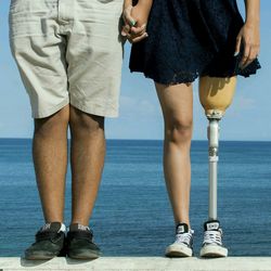 Low section handicapped woman with man standing on retaining wall against sea