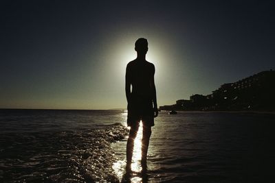 Silhouette man standing on beach against clear sky