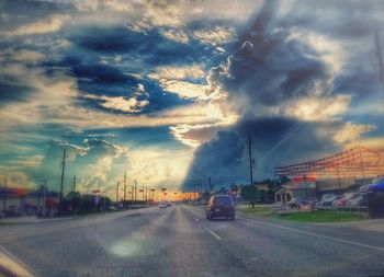 Cars moving on road against cloudy sky