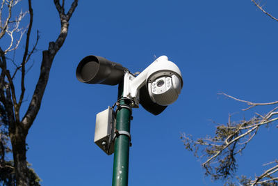 Low angle view of security camera against clear blue sky