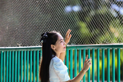 Portrait of a young woman standing against fence