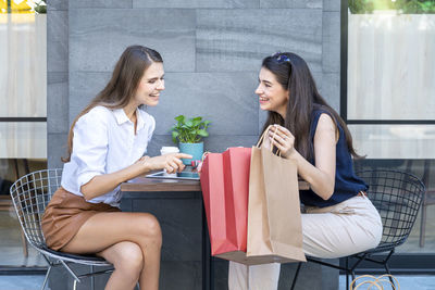 Happy woman paying in cafe by credit card and smart phone. two young woman  in a coffee shop.