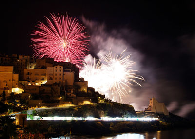 Firework display in city against sky at night