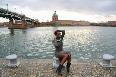 Portrait of beautiful fashion model sitting on bollard by garonne river in city