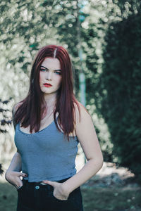 Portrait of beautiful young woman standing against trees