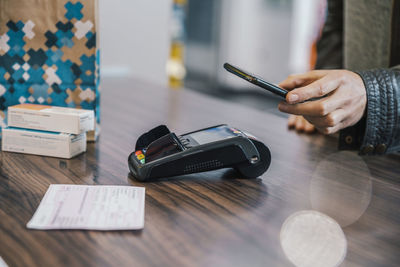 Hand of customer with smart phone at checkout counter in chemist shop