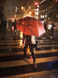 Low section of woman with red umbrella walking on road during rainy season