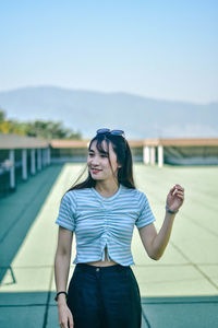 Young woman smiling while standing on floor at building terrace against sky