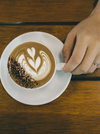 Cropped hand of woman holding coffee on table