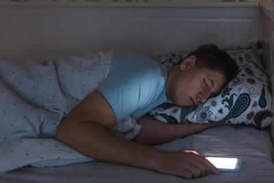 Man falling asleep with phone holding in hand at night in bed. internet and cell phone addiction.