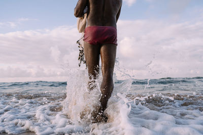 Shirtless fisherman walking with fishing net towards sea against sky