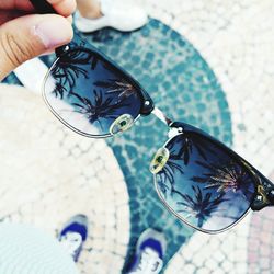 Close-up of hand holding sunglasses with reflection of palm trees