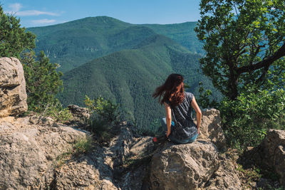 Full length of man sitting on rock against mountains