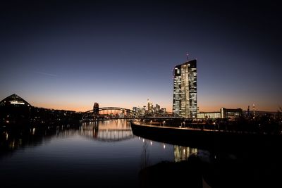 Illuminated buildings by river against sky at night