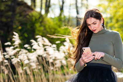 Woman using phone while standing on tree