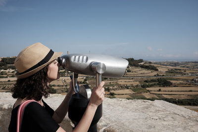 Woman looking through coin-operated binoculars against sky