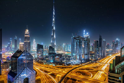 Illuminated burj khalifa amidst buildings in elevated road at night