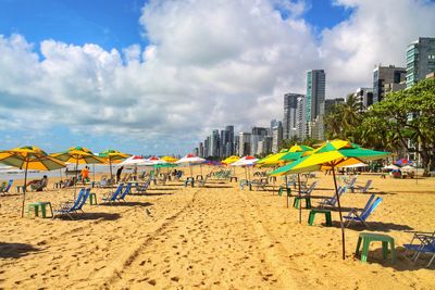 Hooded chairs on beach against sky in city