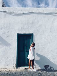 Full length of young woman standing against whitewashed house