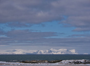 Scenic view of sea by snowcapped mountains against sky