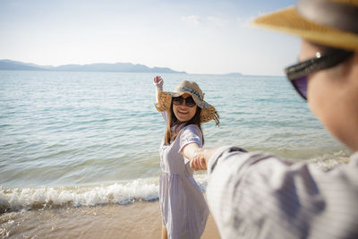 Smiling woman holding hand of boyfriend at beach